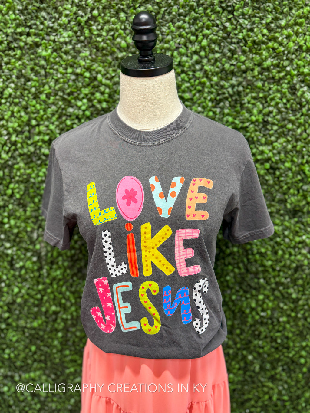 Gray t-shirt with colorful text on a mannequin against a green textured wall.
