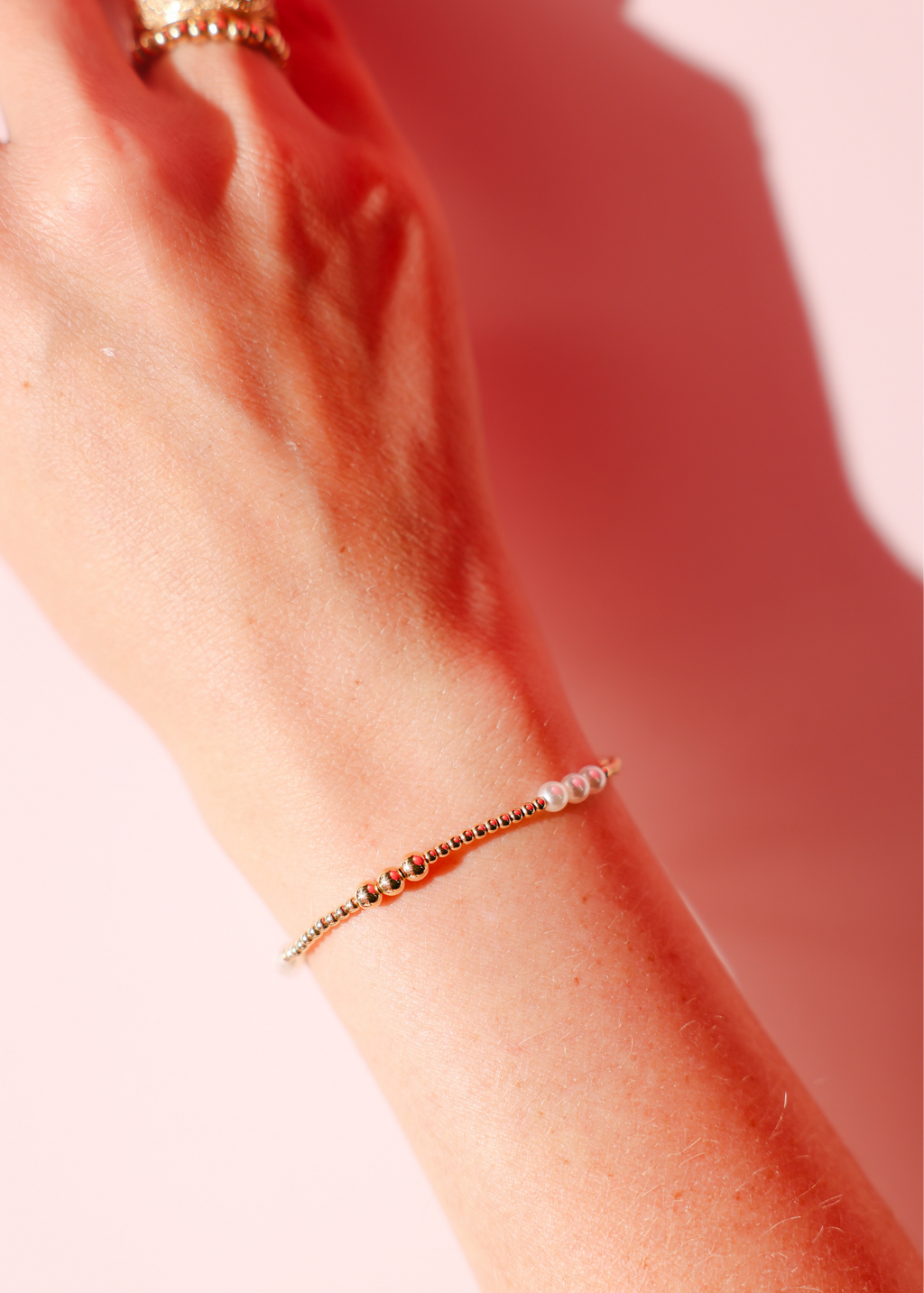 Close-up of a wrist wearing a beaded bracelet against a pink background