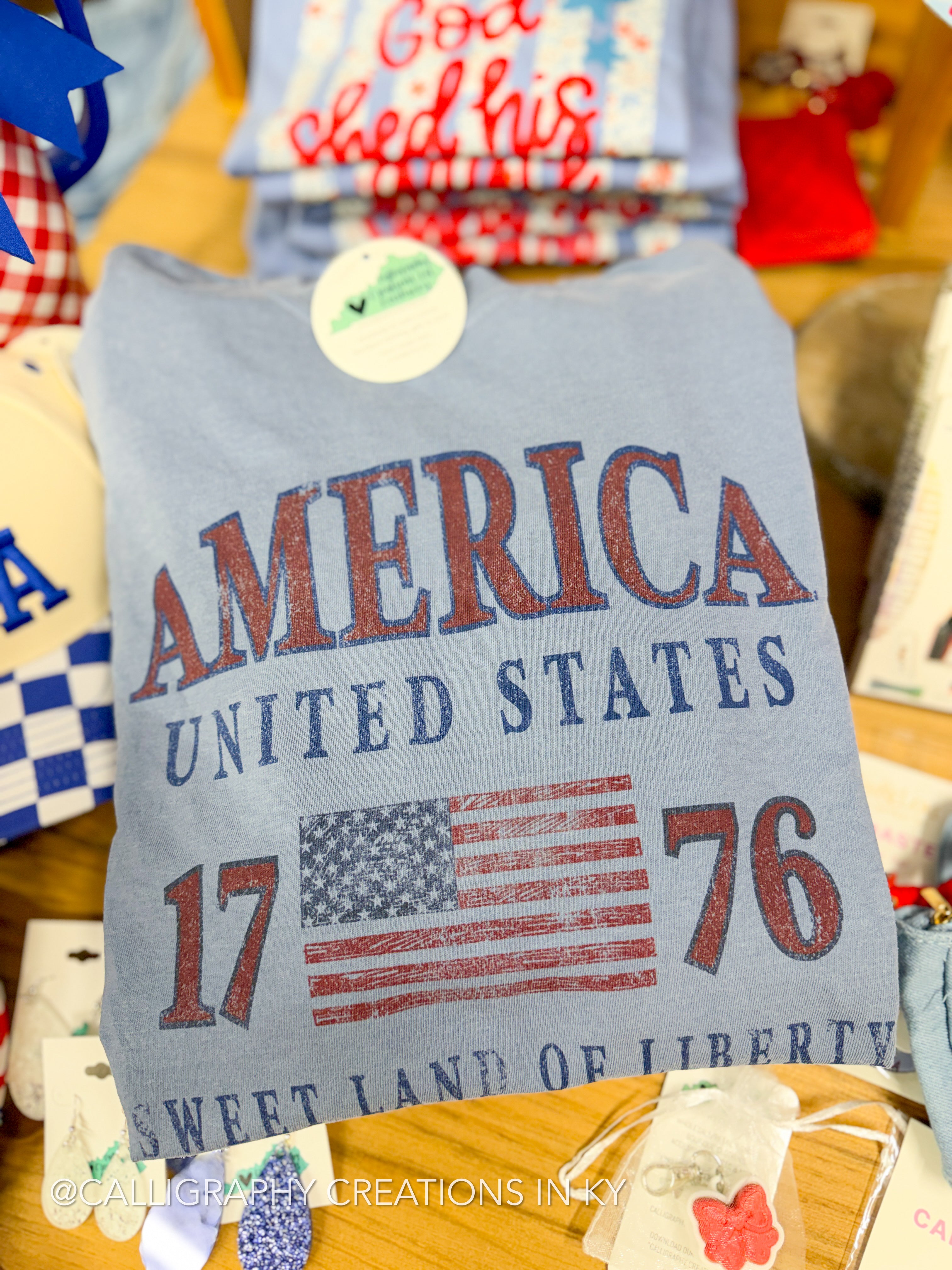 Gray t-shirt with 'America United States 1776' text and flag design on a table with various items.