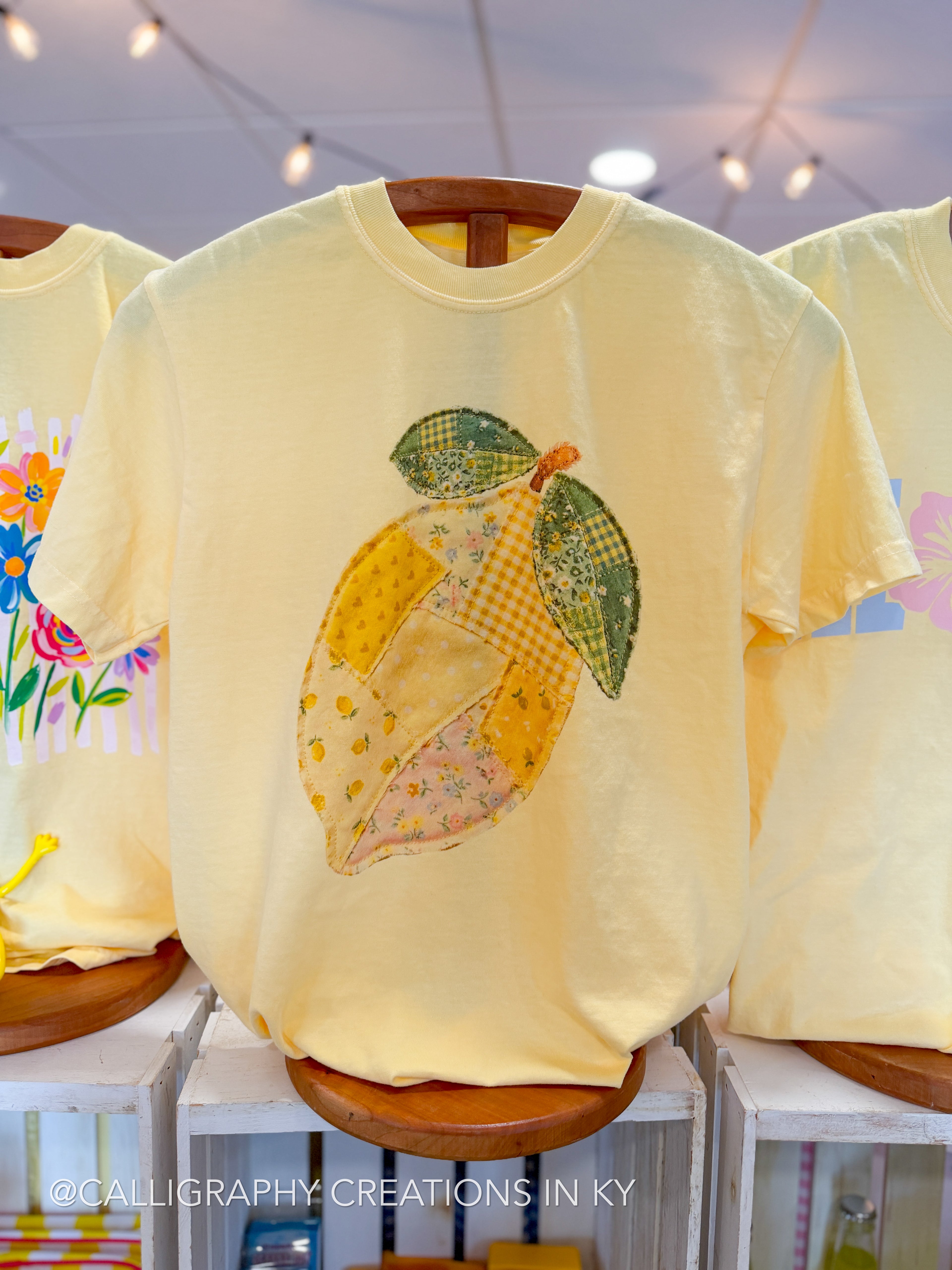Yellow sweatshirt with a patchwork lemon design on a wooden hanger.