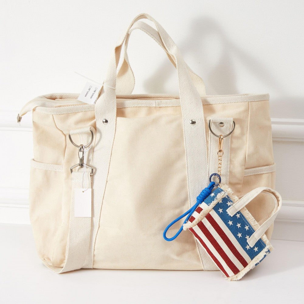 Miniature American flag handbag shown as a bag charm on a larger white duffel bag. 