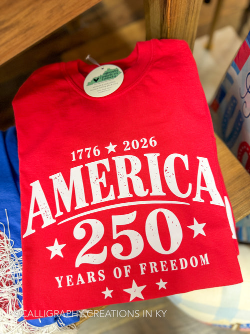 Red t-shirt with 'America 250 Years of Freedom' text on a wooden surface