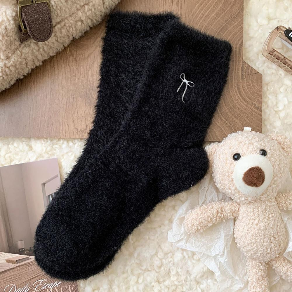Black fuzzy socks with a teddy bear and books on a soft surface