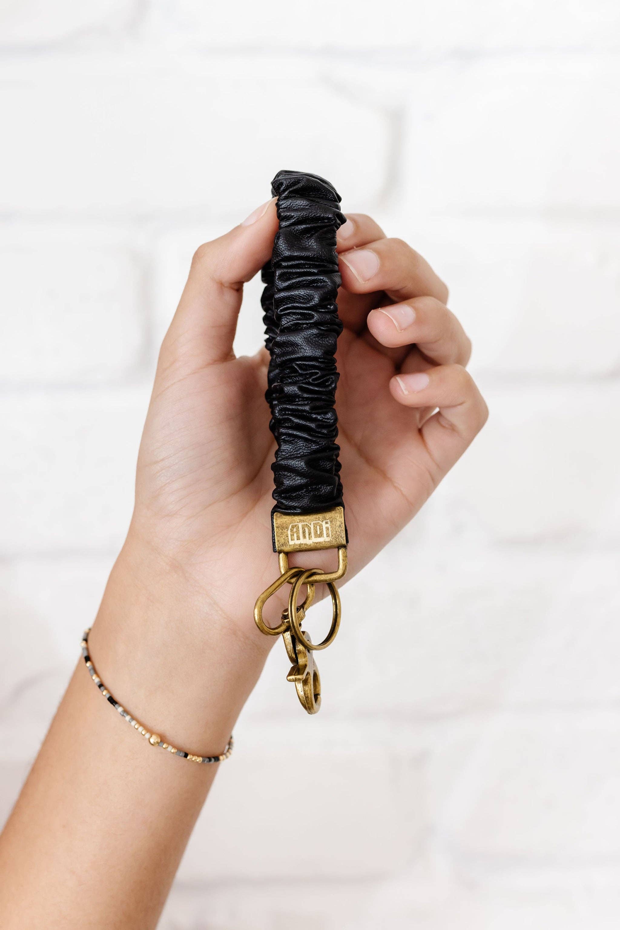 Hand holding a black scrunchie keychain with gold clasp on a white background