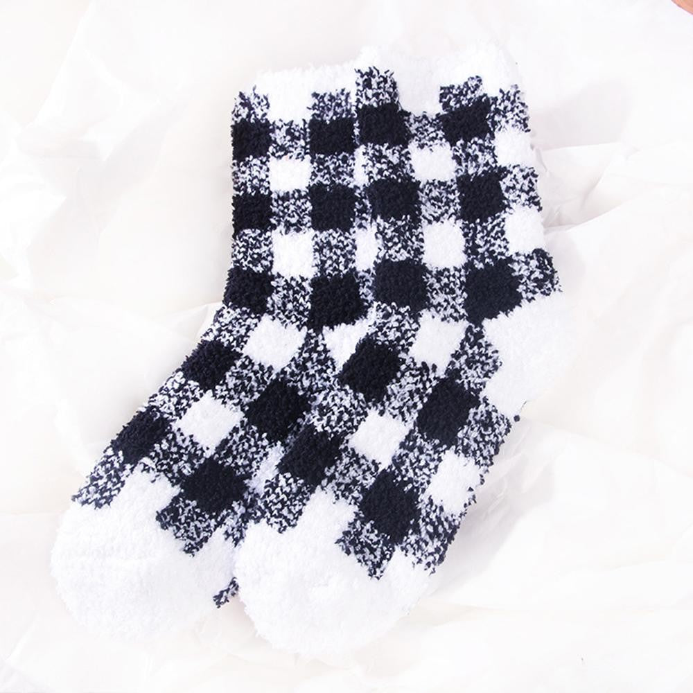 A pair of fuzzy black and white checkered socks laid flat on a white fabric background.
