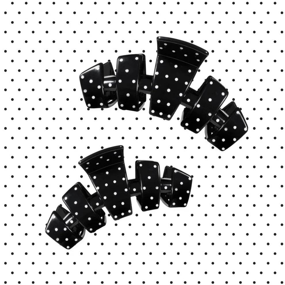 Two black hair claw clips with white polka dots, arranged on a white background with a black polka dot pattern.