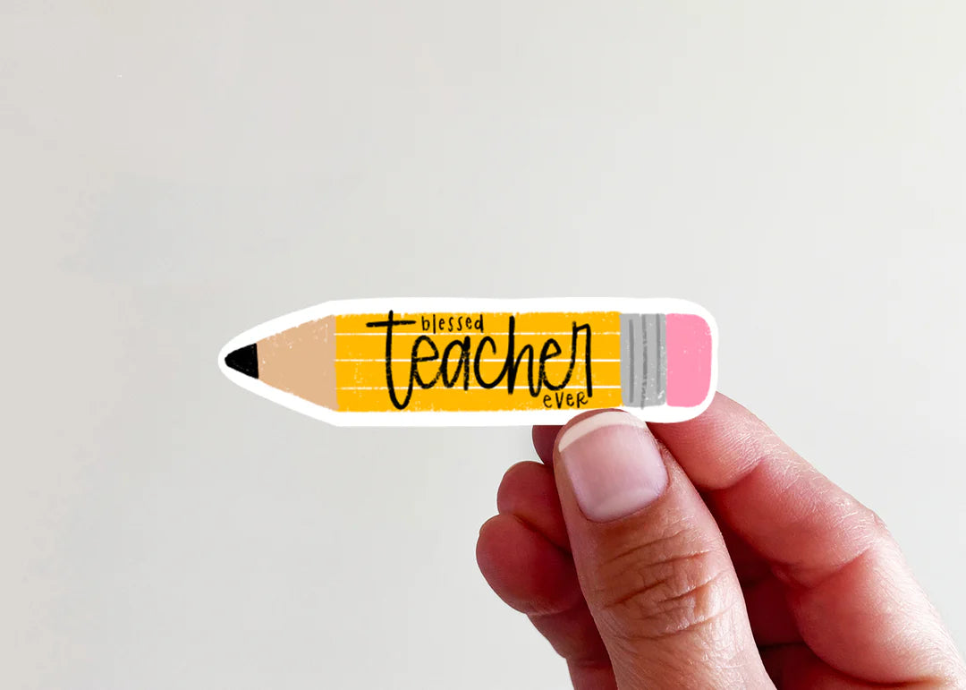 A hand holding a die-cut sticker shaped like a pencil with the words 'blessed teacher ever' in black script on a yellow striped body, against a plain light background.