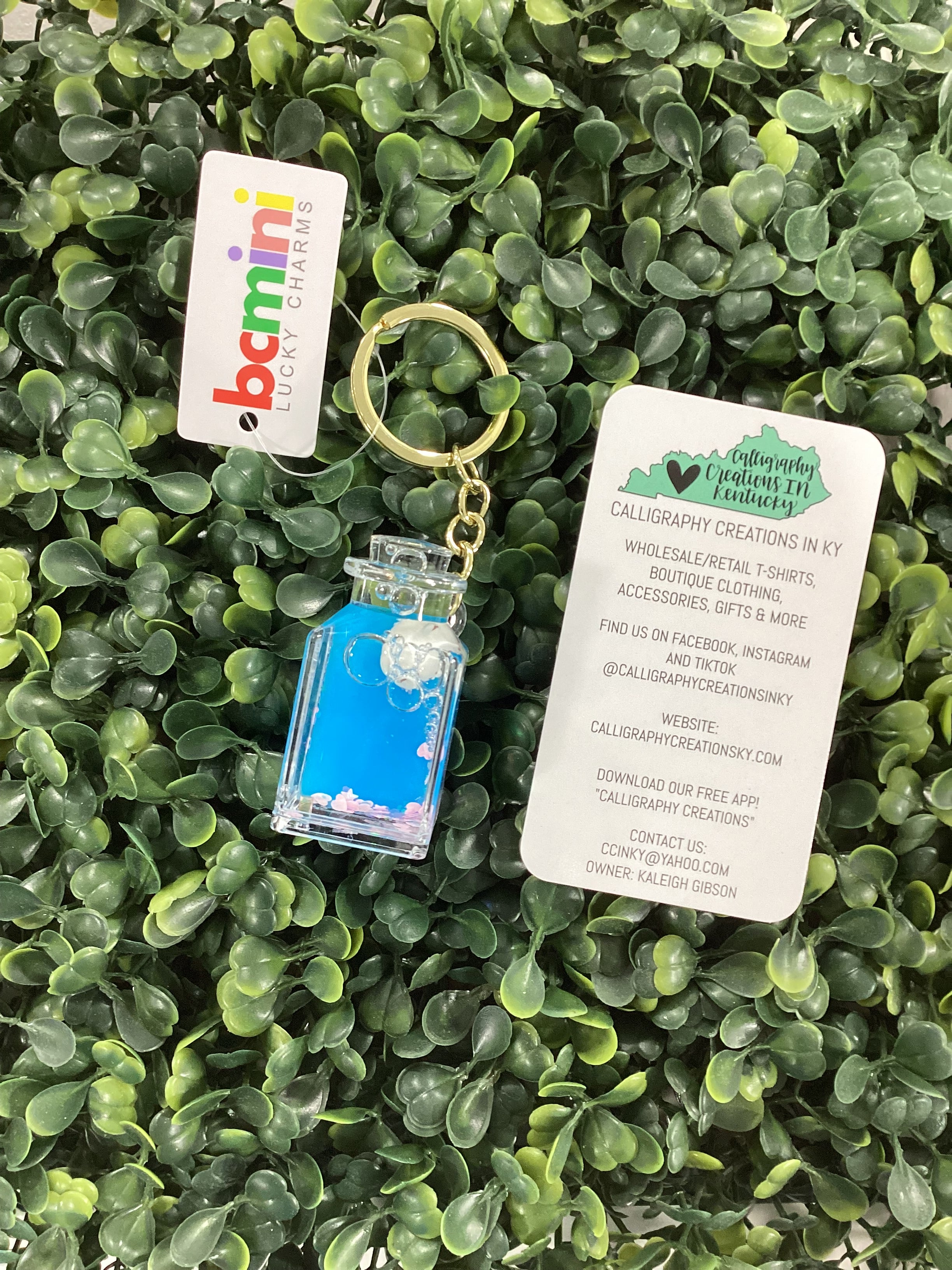 Keychain with blue liquid and small plastic cat on the inside on green artificial grass