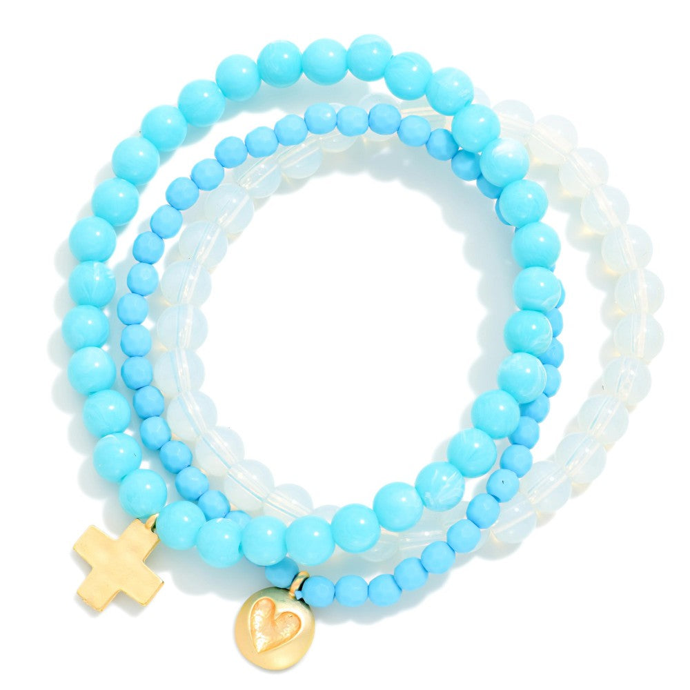 Set of light blue beaded bracelets with gold charms on a white background