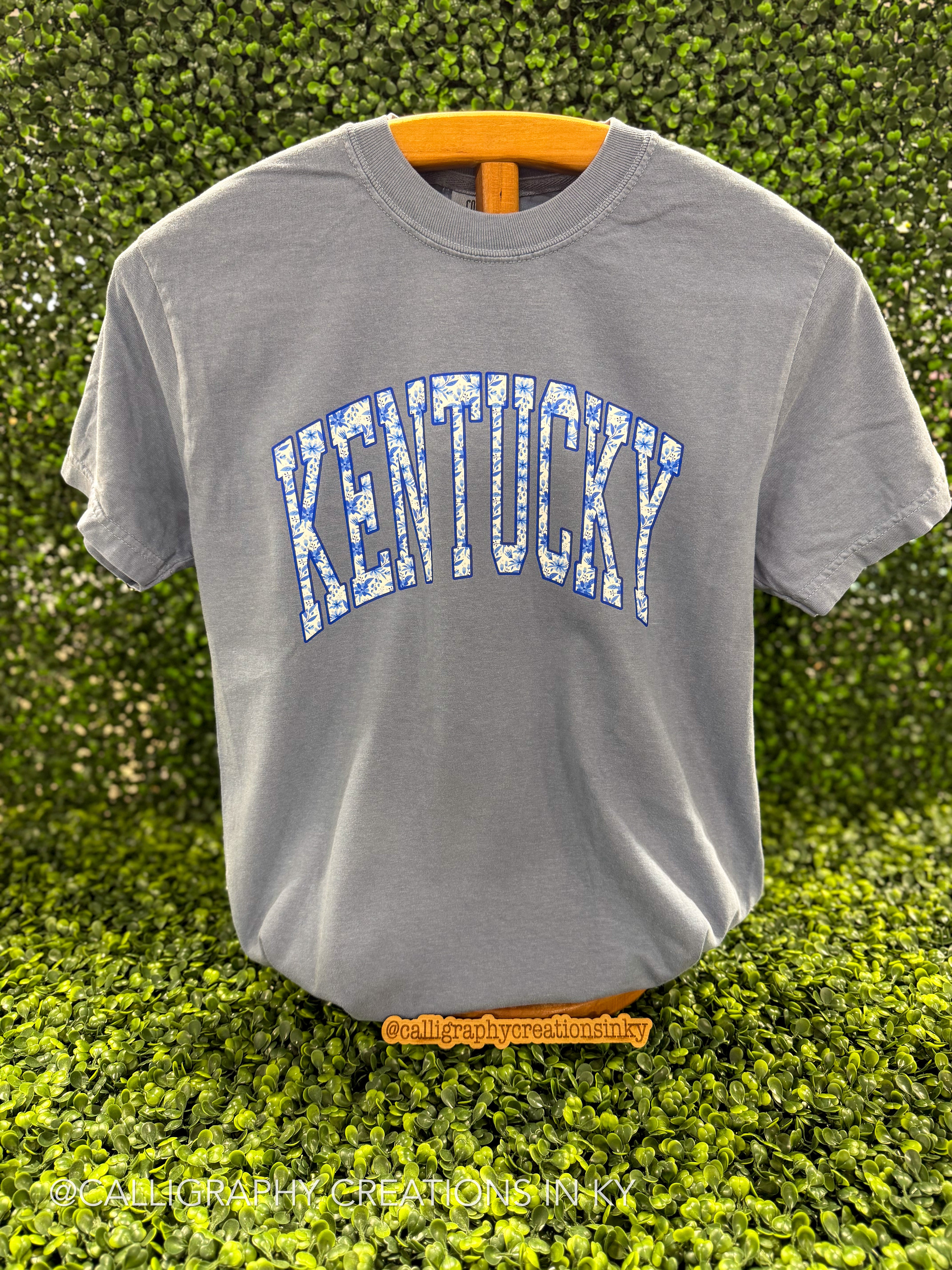 Picture of a Blue Floral Arch Kentucky CC Tee with a grass background 