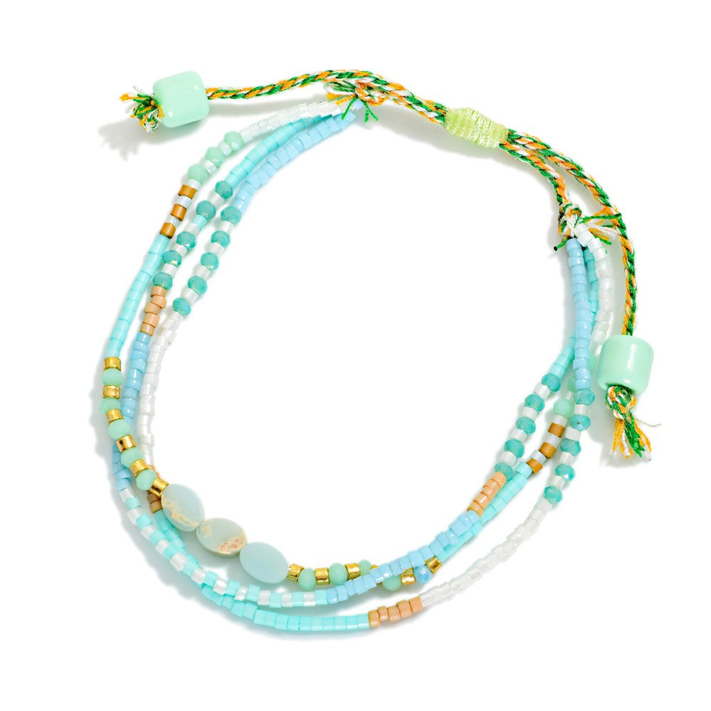 Multistrand beaded necklace with turquoise, gold, and white beads on a white background