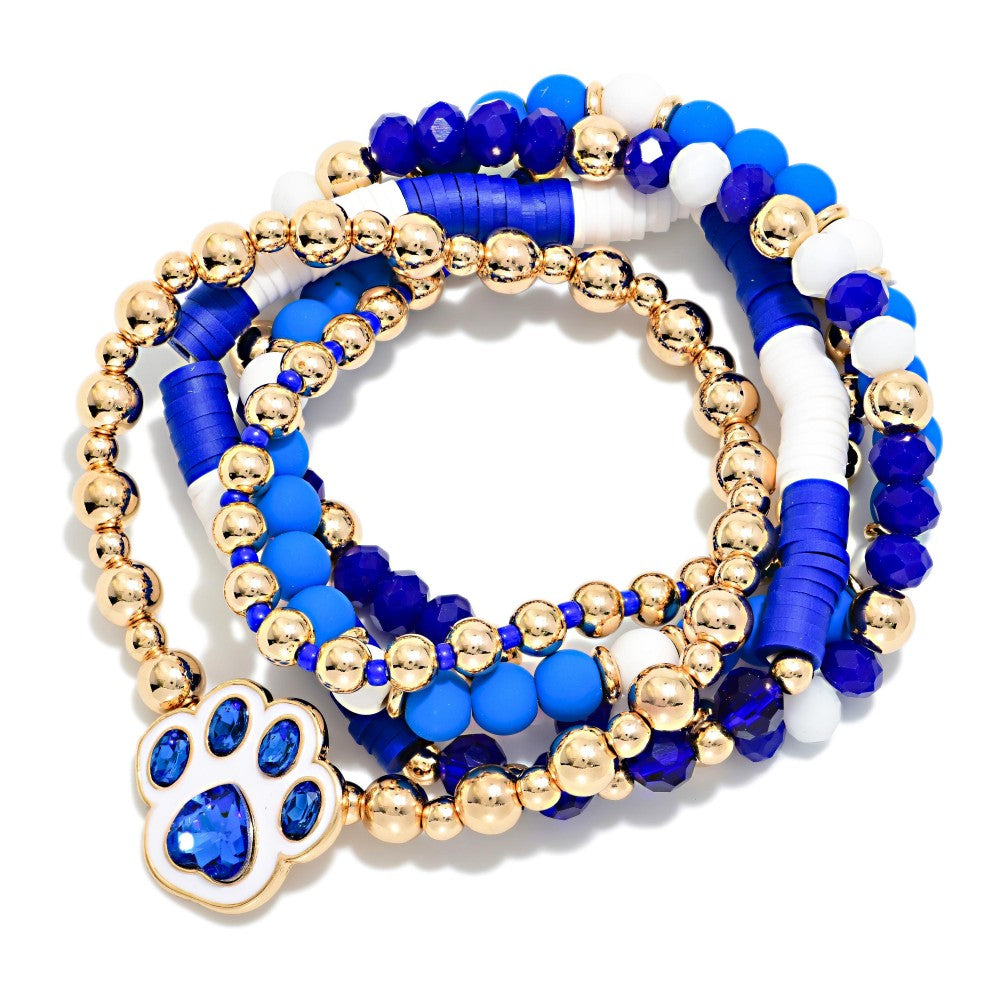 A set of multi-strand beaded stretch bracelets featuring royal blue, cobalt blue, white, and metallic gold beads, with a gold-plated paw print charm embellished with blue rhinestones, displayed on a clean white background.