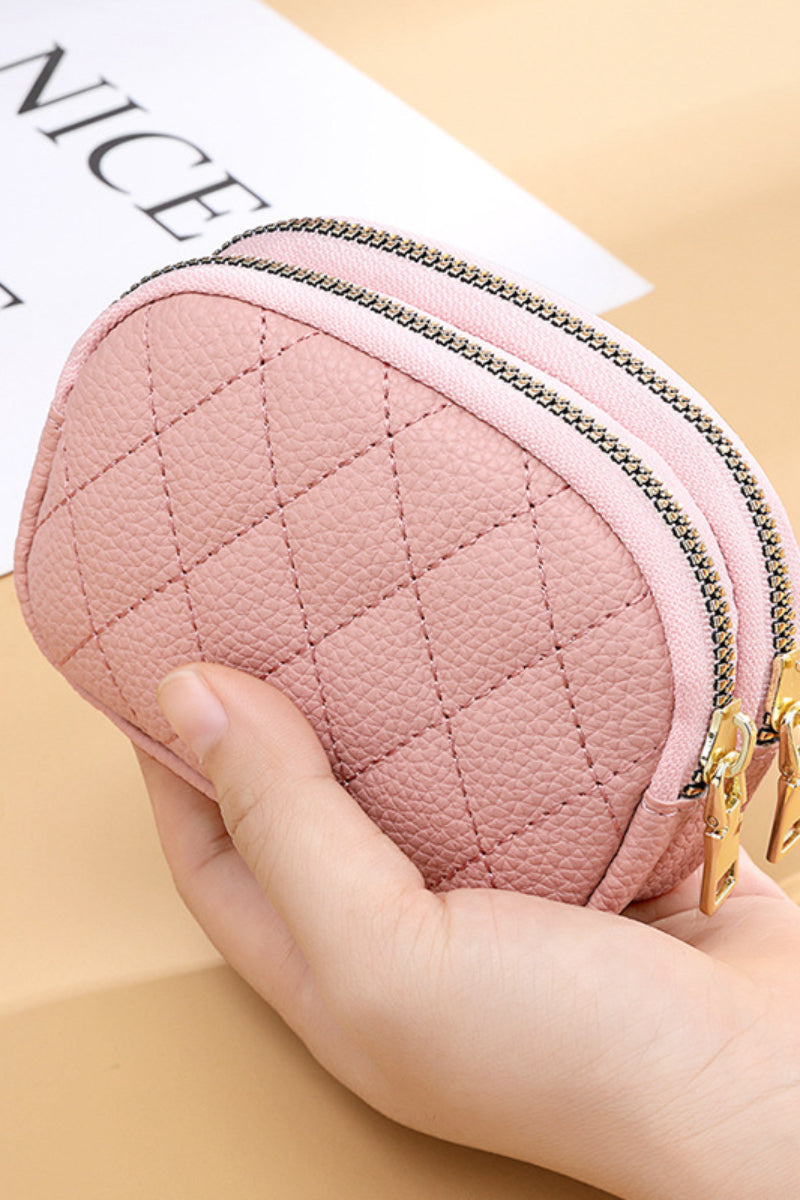 Light pink coin purse with gold double zippers in a hand against a wood background