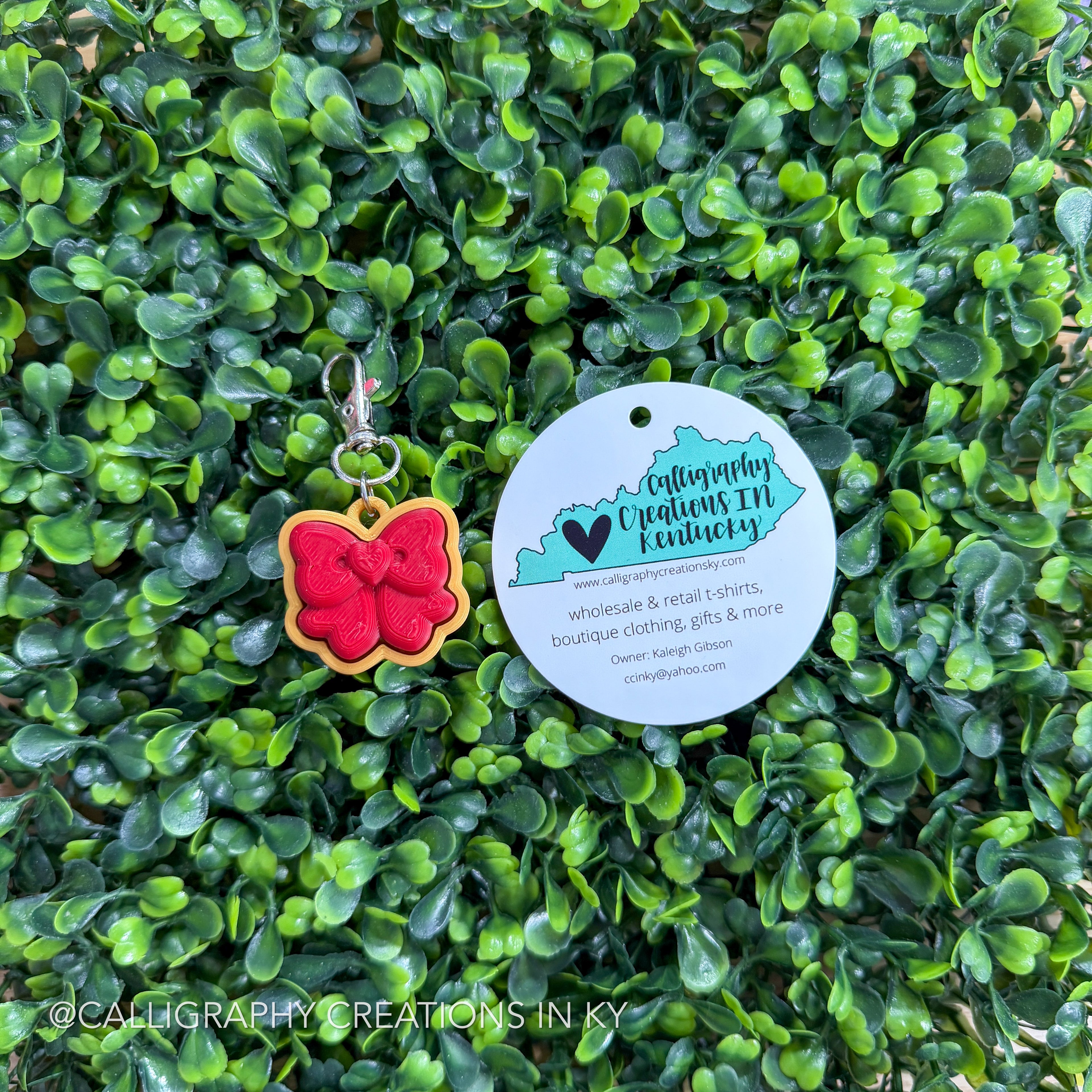 Bow shaped fidget clicker keychain with a tag on a green leafy background