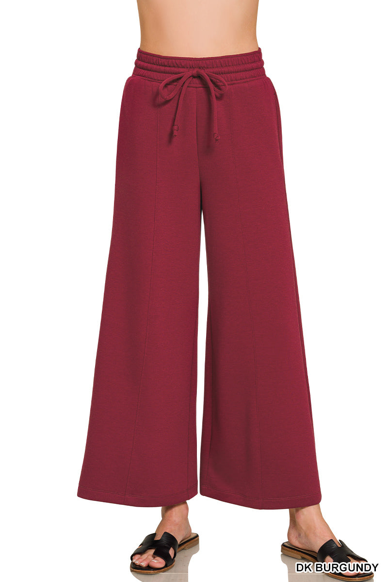 A person wearing wide-leg drawstring pants in a deep burgundy color, paired with black slide sandals, shown against a plain white background.