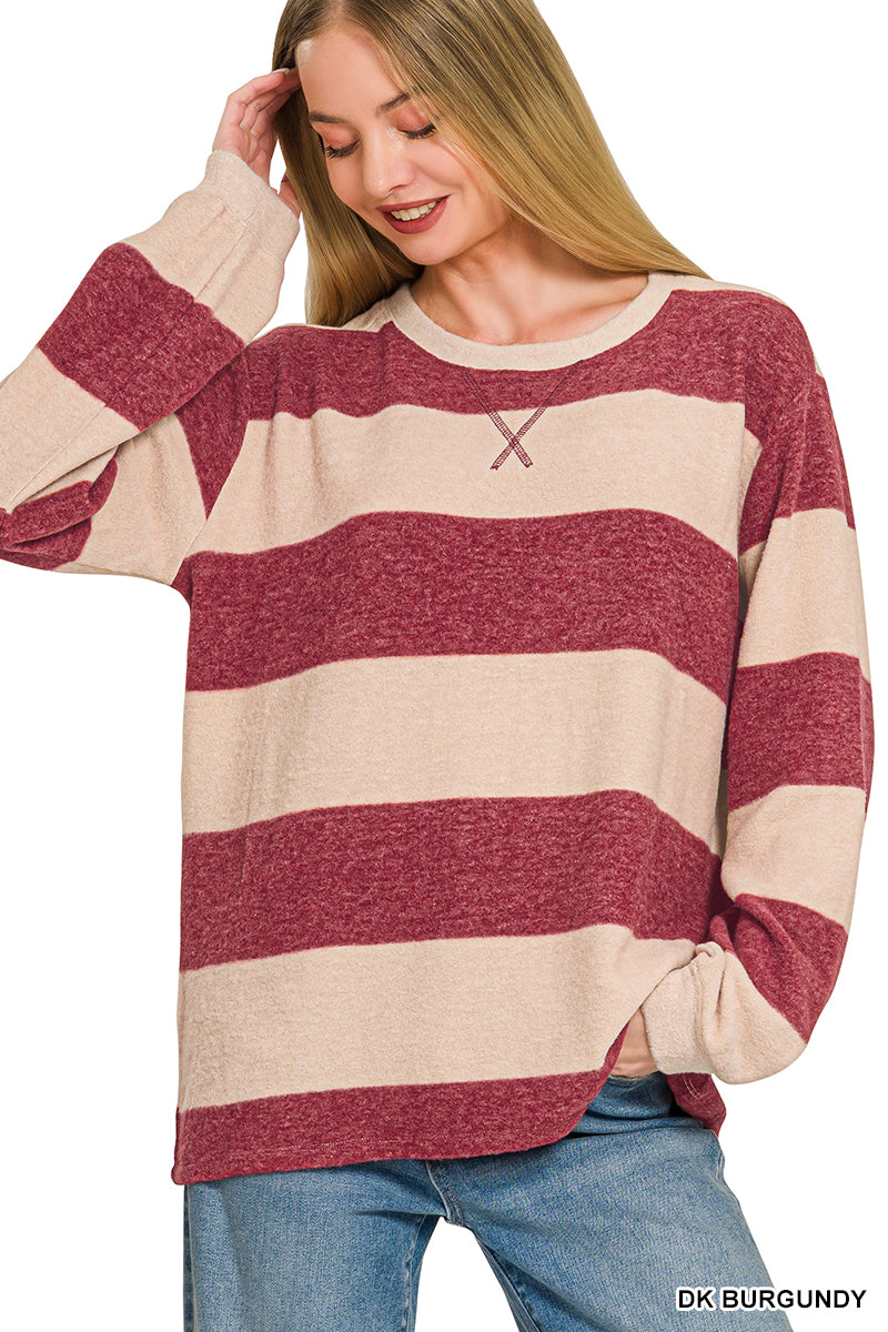 A woman wearing a heathered burgundy and beige striped long-sleeve knit sweater with a small embroidered 'X' logo on the chest, paired with blue jeans.