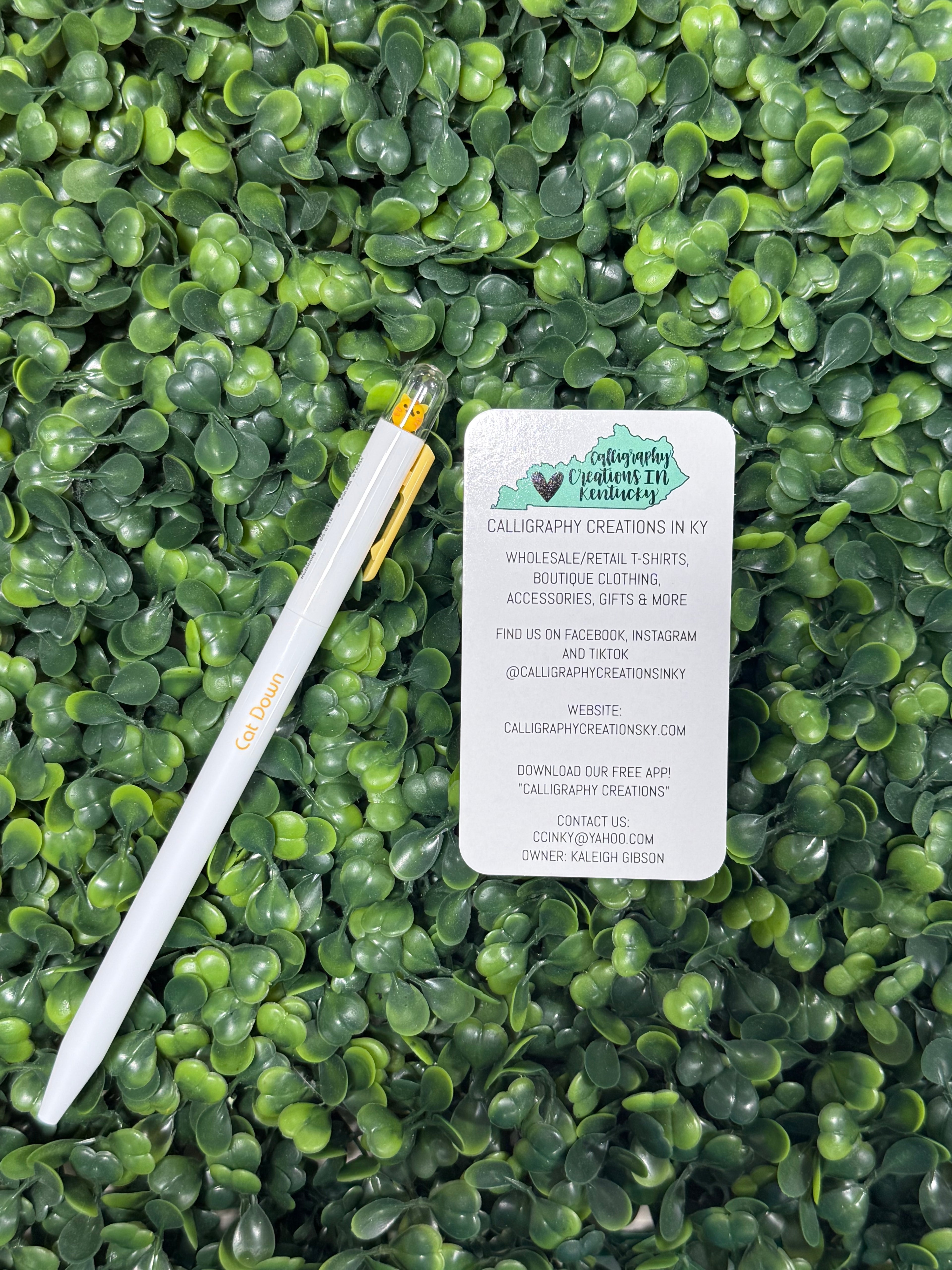 White pen with yellow cat on top on a green leafy background