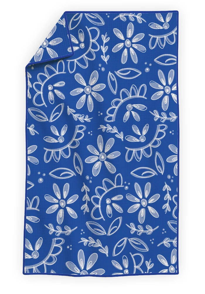 A rectangular blue towel or blanket with a white floral and leaf pattern, shown flat against a white background with one corner folded over.