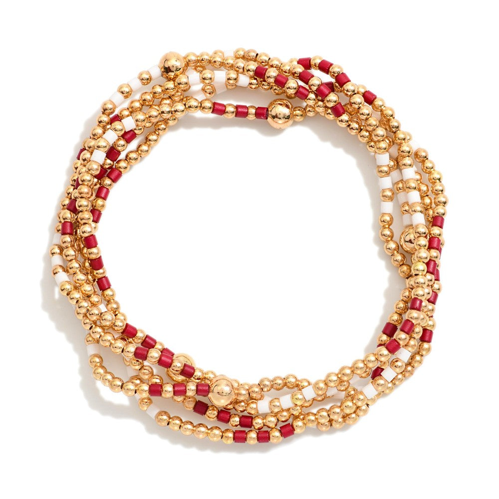 A multi-strand beaded wrap bracelet featuring gold-tone metallic beads and alternating red cylindrical beads, arranged in a circular loop on a white background.