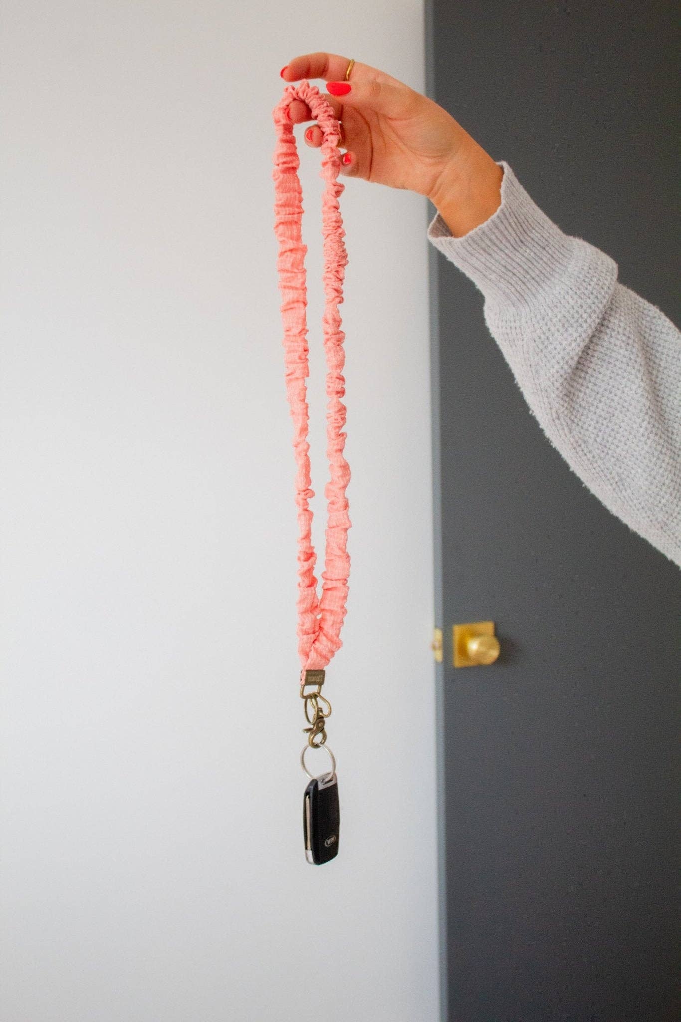 Hand holding a coral scrunchie lanyard with a keychain against a neutral background