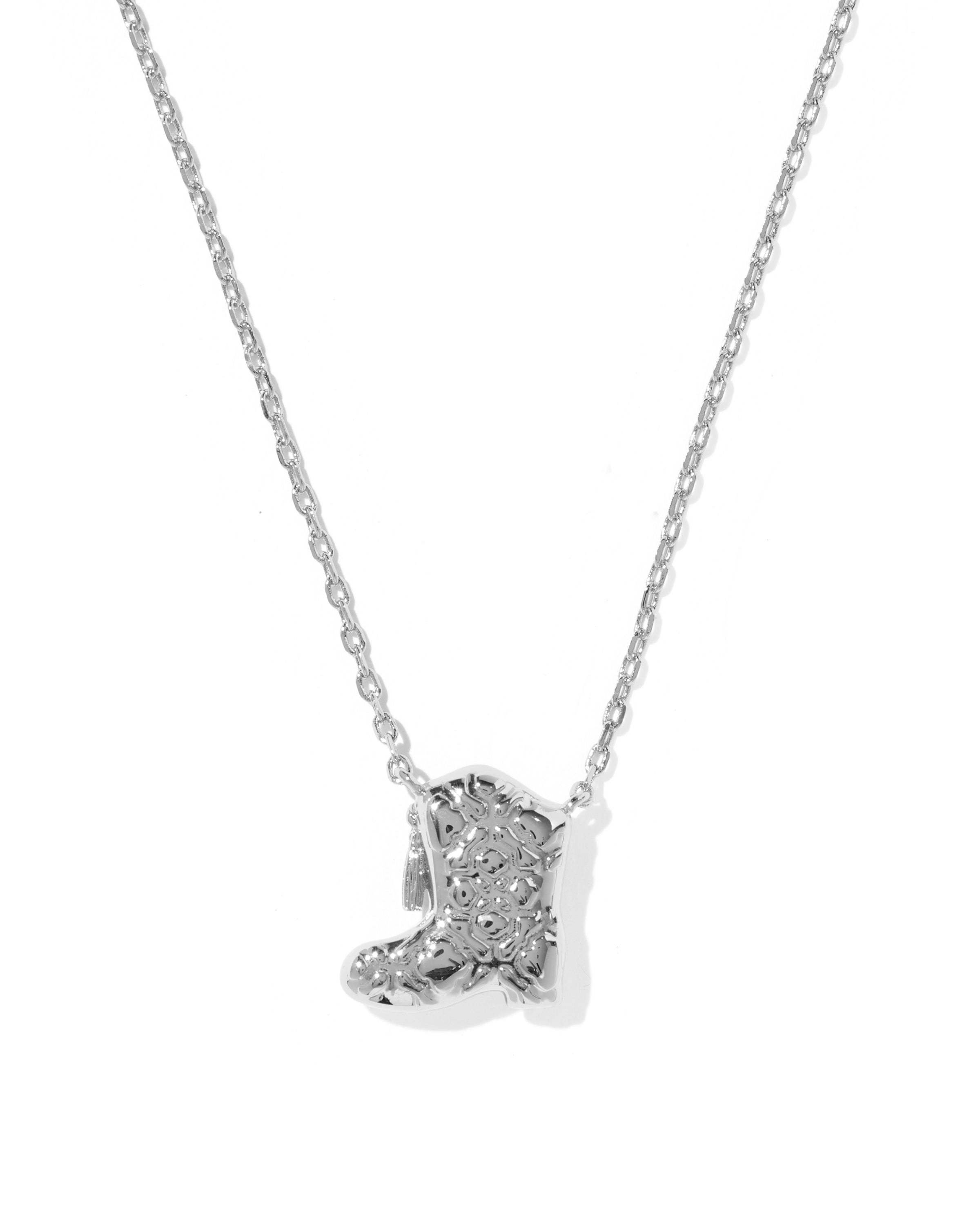 A silver-toned necklace featuring a small boot-shaped pendant paved with clear stones, shown against a plain white background.