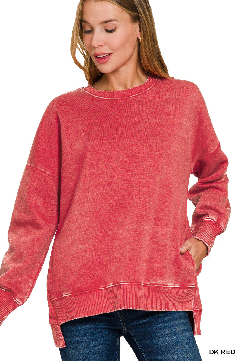 A woman wearing a washed red crewneck sweatshirt with long sleeves and ribbed cuffs, hem, and collar, paired with blue jeans against a white background.
