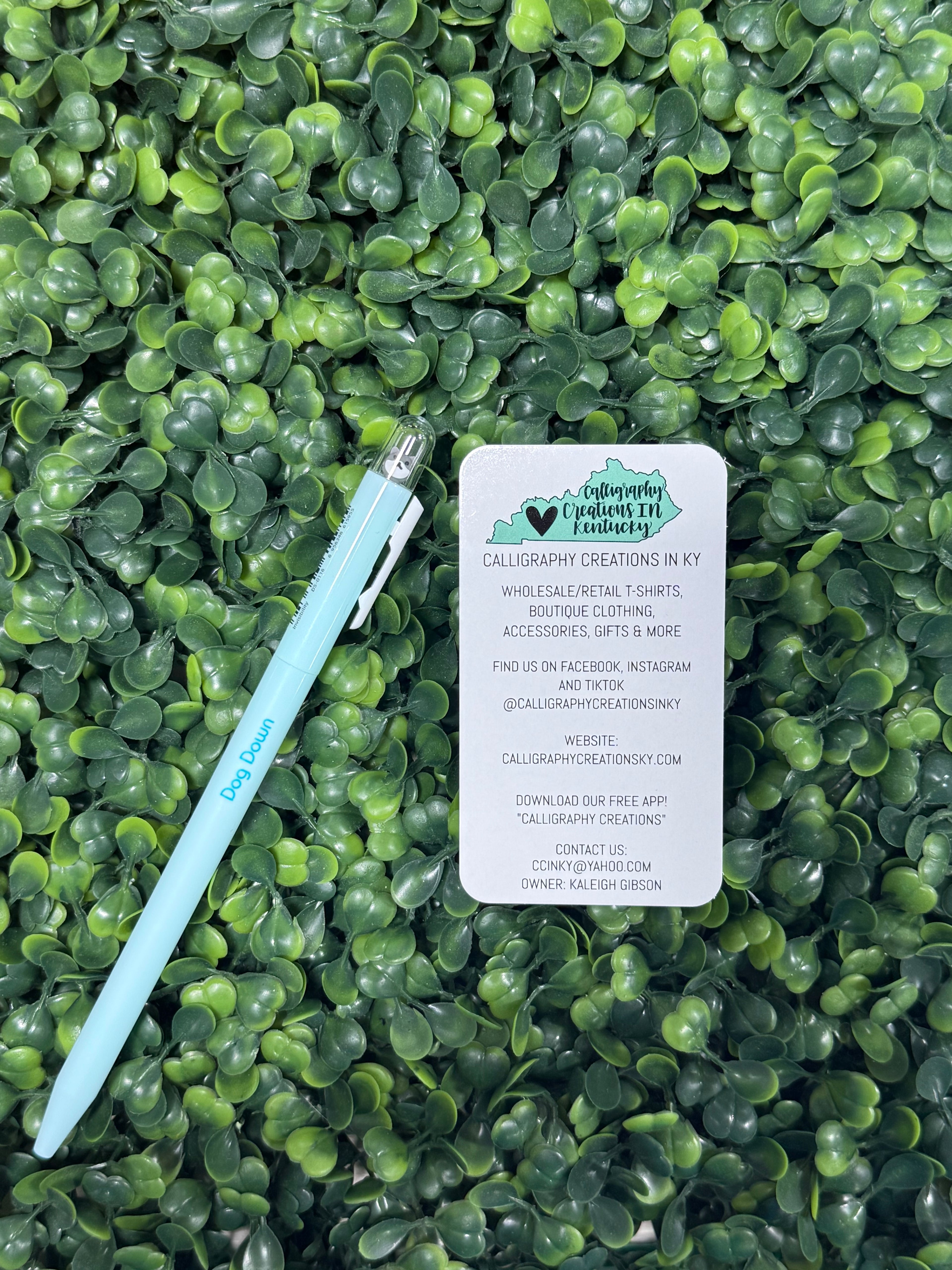 Light blue pen and business card on a green leafy background