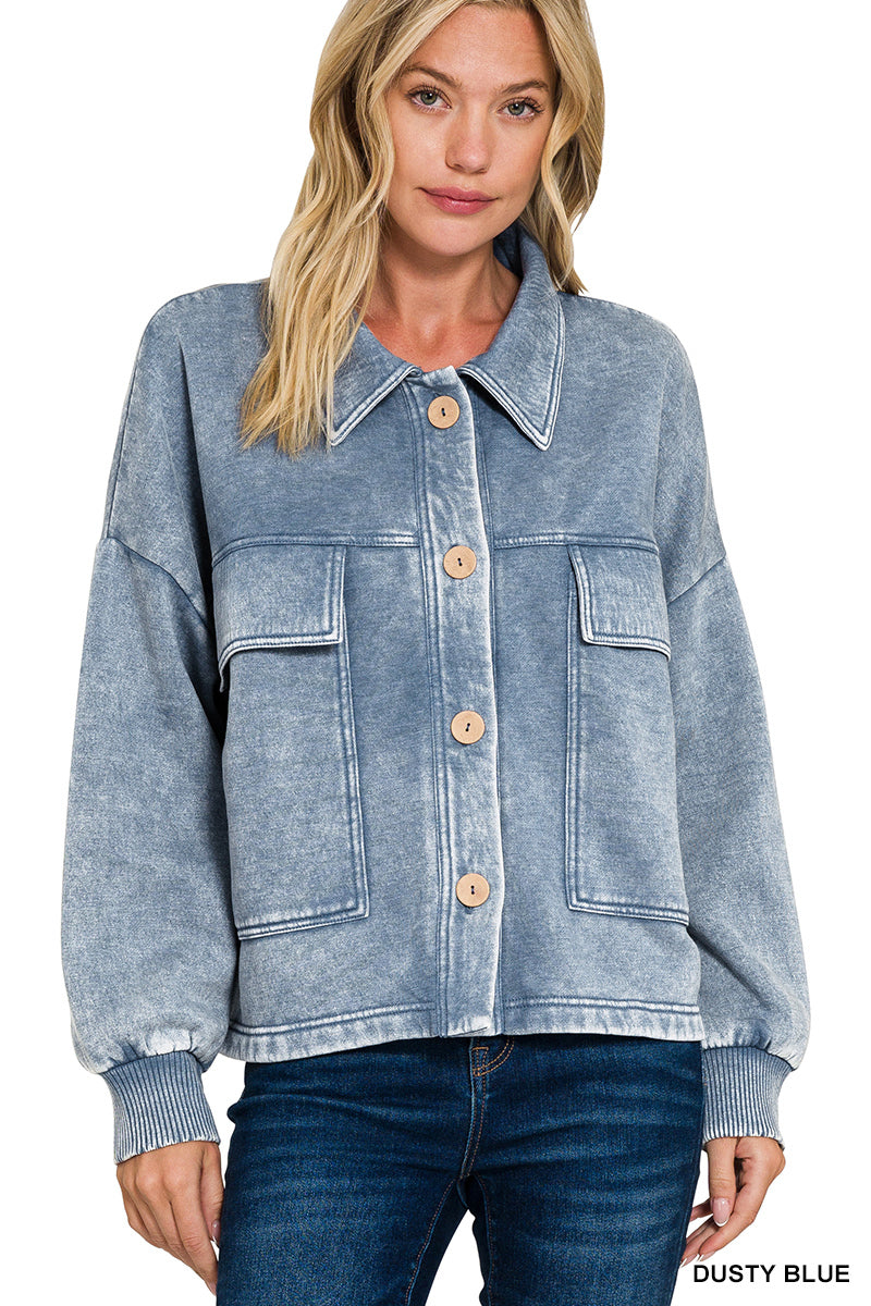 A woman wearing a light blue acid-wash blue jacket with four large front flap pockets and wooden buttons, paired with dark blue jeans against a plain white background.