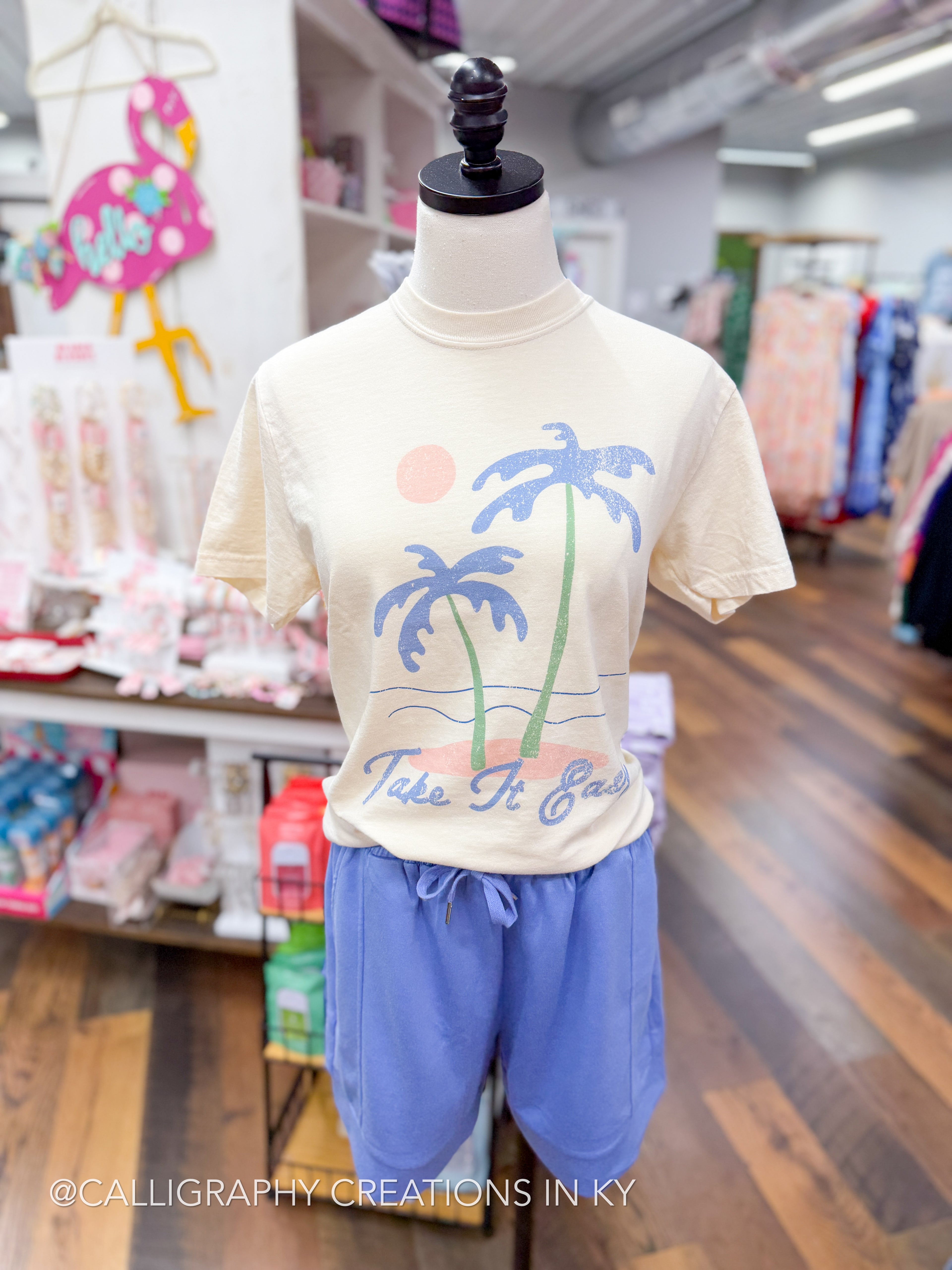 Mannequin wearing a cream t-shirt with palm tree design and blue shorts in a store setting.