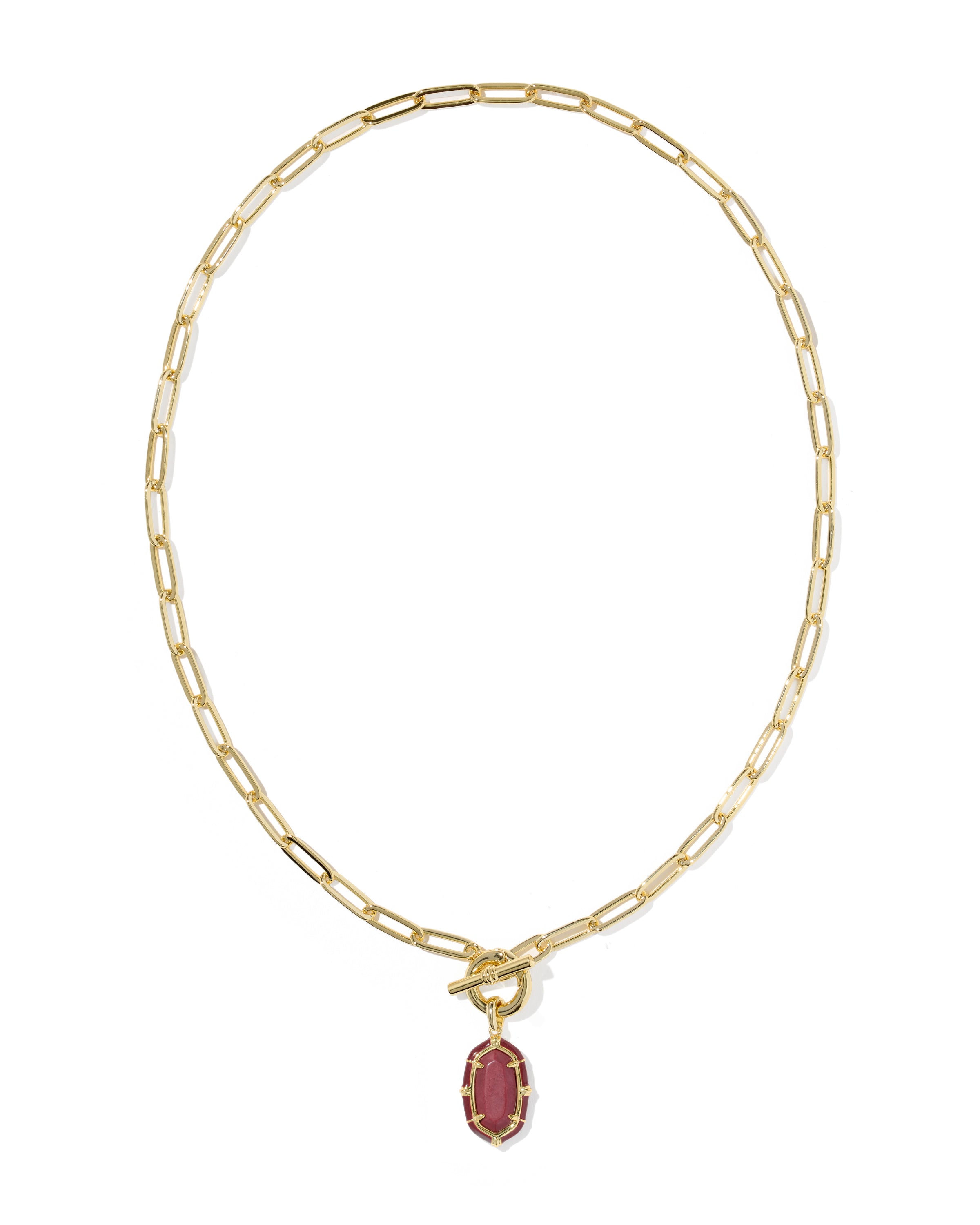 A gold paperclip chain necklace with a toggle clasp and a small oval pendant featuring a dark red center stone surrounded by a gold border, shown on a plain white background.