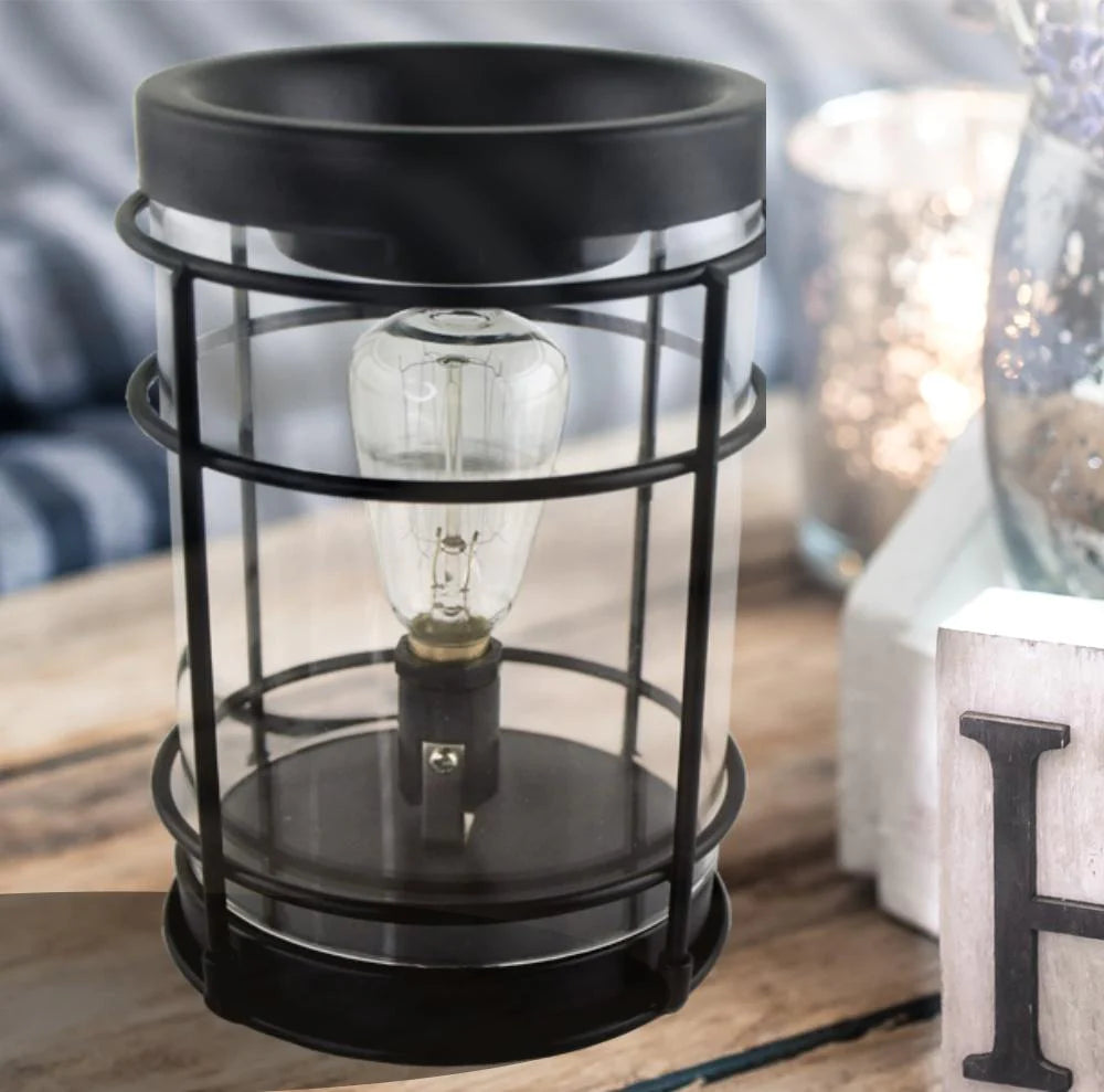 A black ceramic candle warmer with an Edison light bulb, placed on a wooden surface.