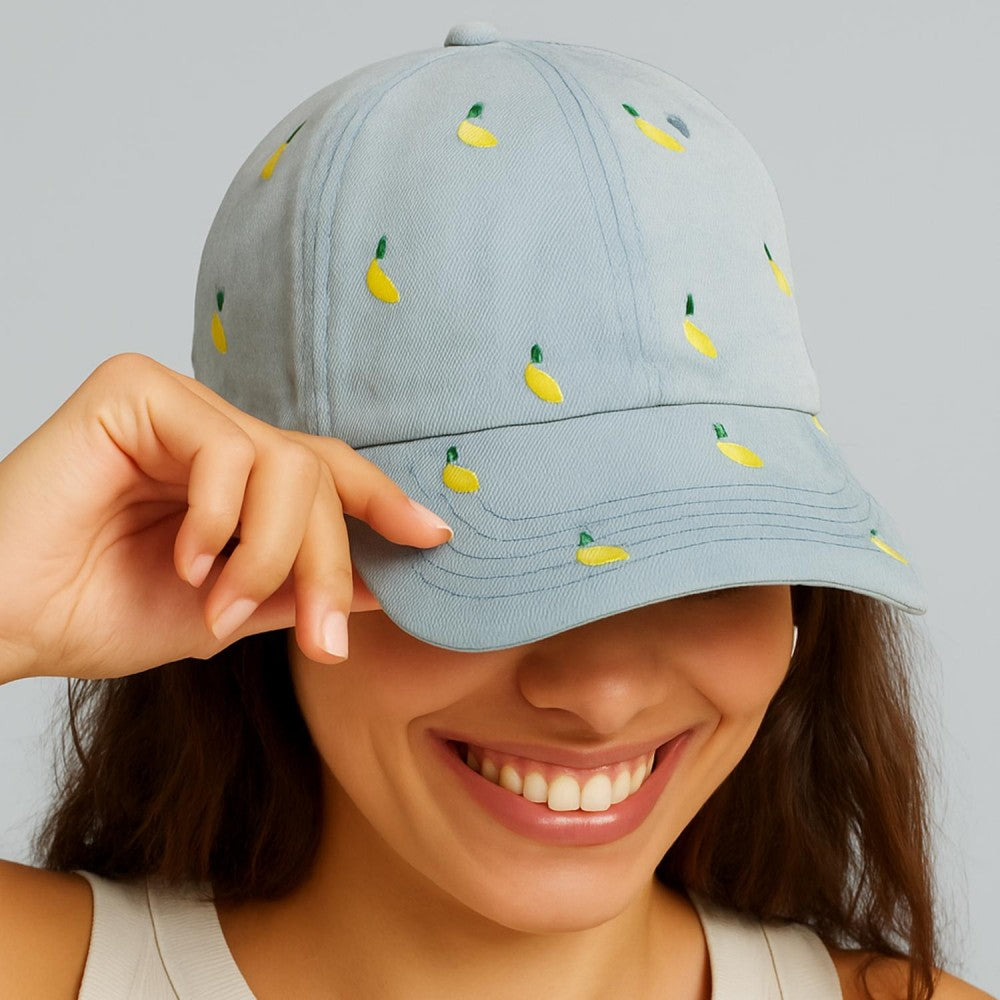 Person wearing a light blue cap with embroidered banana designs on a plain background
