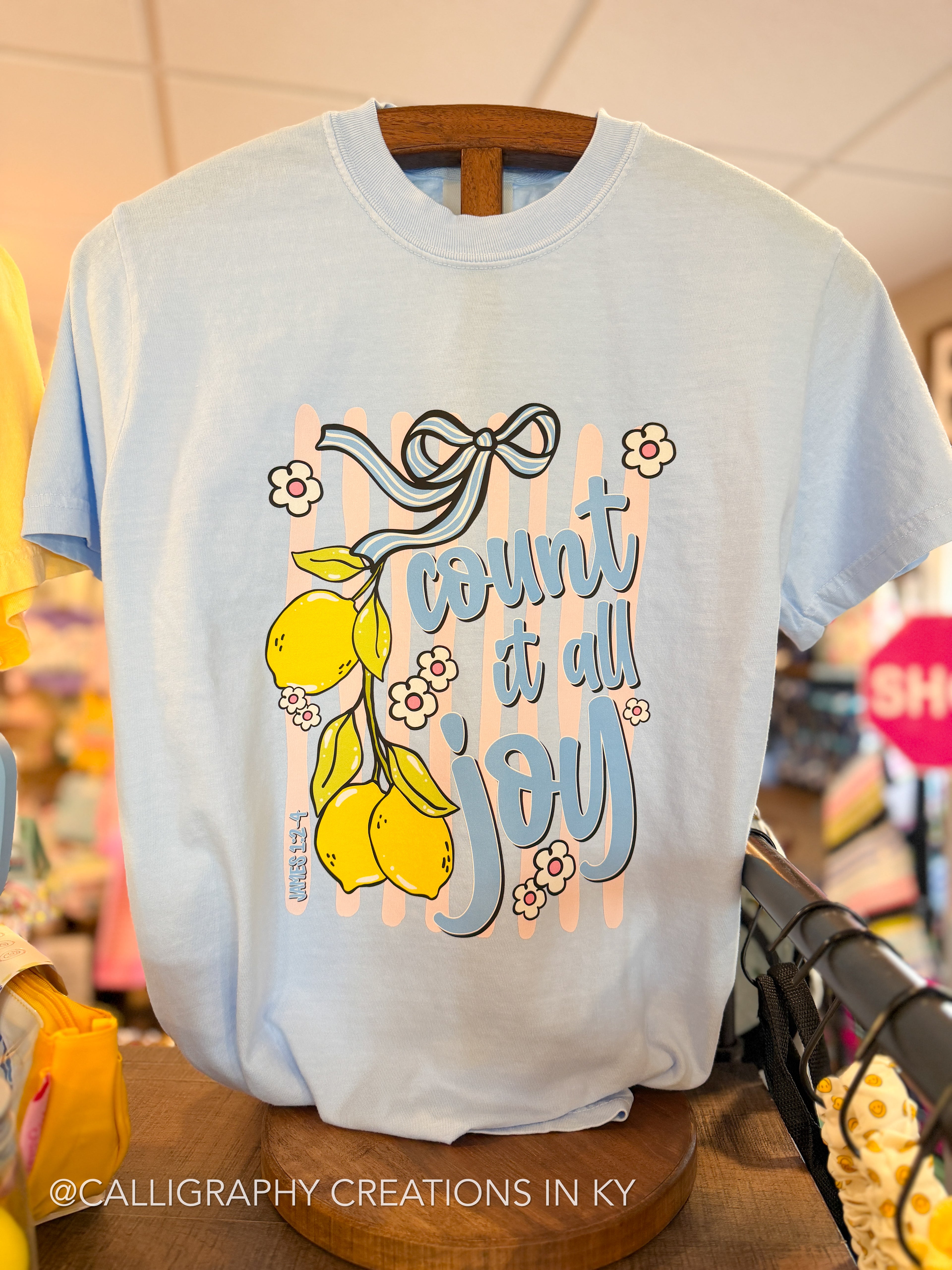Light blue t-shirt with 'count it all joy' design on a wooden hanger.