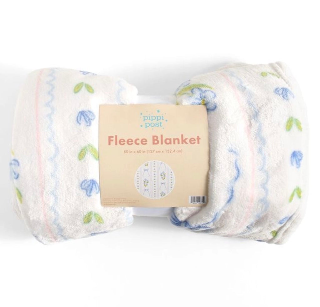 A folded fleece blanket with a cream base, decorated with light blue floral motifs, green leaves, and pastel pink and blue wavy stripes. The blanket is wrapped in its original paper packaging label, which reads 'pippi + petra Fleece Blanket'.