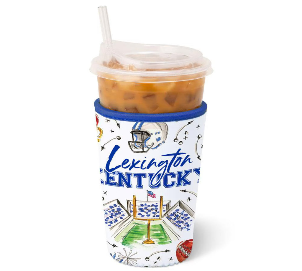 A clear plastic insulated tumbler with a clear lid and straw, filled with an iced orange-brown drink, wrapped in a white Lexington Kentucky football-themed sleeve with blue lettering and illustrated stadium graphics.