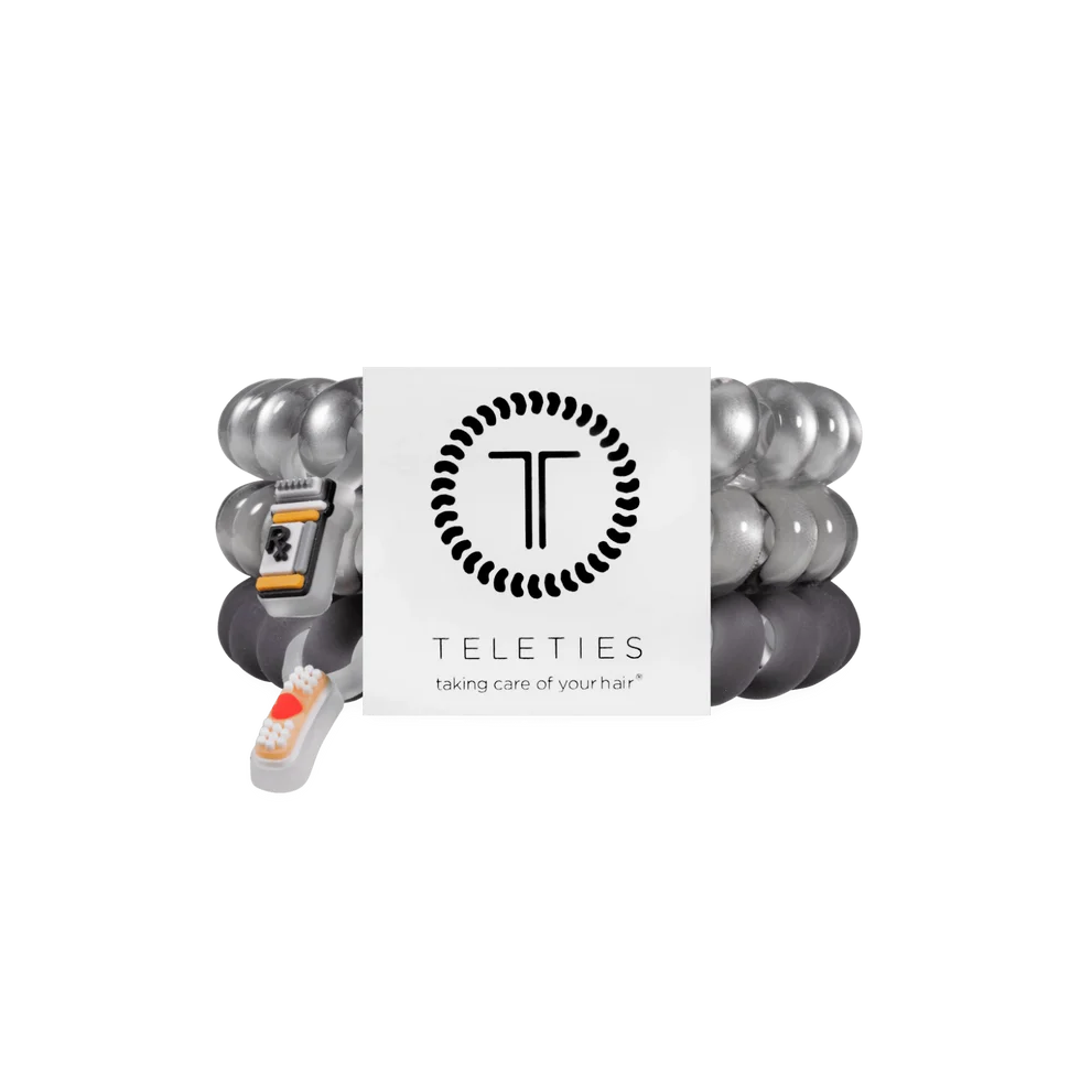 Three coiled hair extension bands in metallic silver, dark gray, and black, bundled with a white Teleties brand card and a small white remote control, on a plain white background.