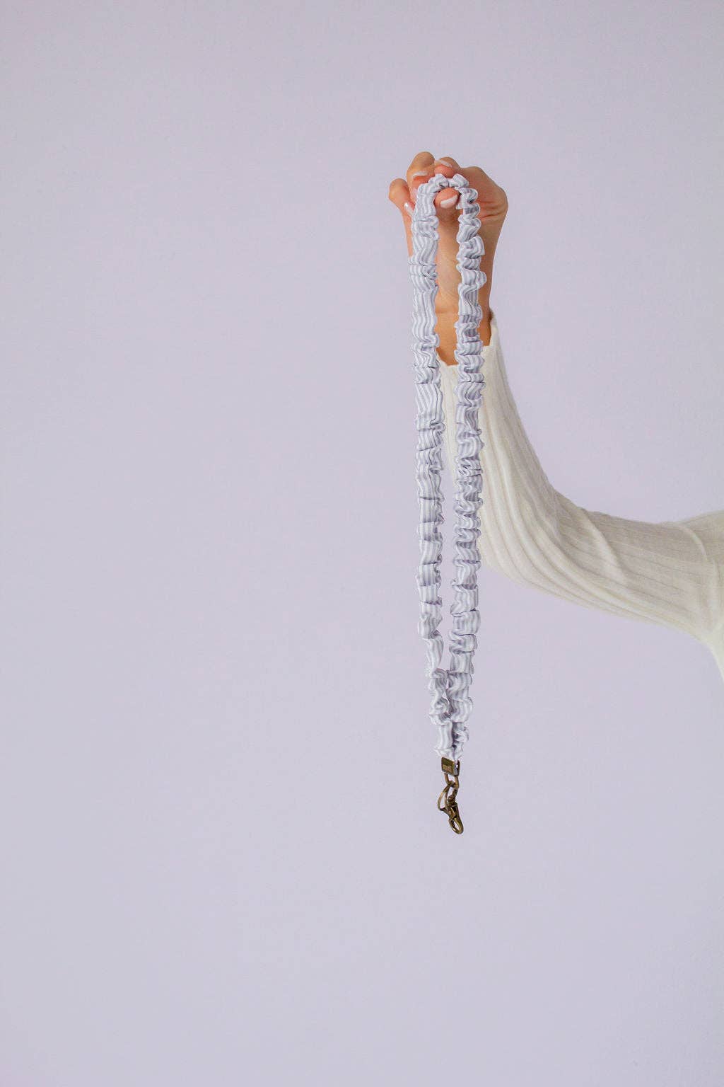 Person holding gray and white striped scrunchie lanyard against a lavender background. 