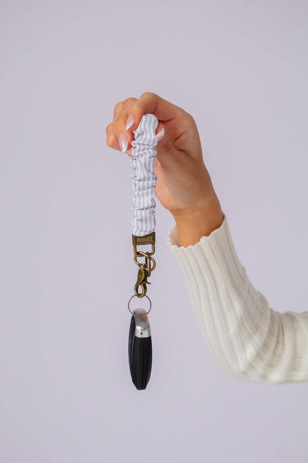 Woman holding gray and white striped scrunchie key chain in front of a lavender background 