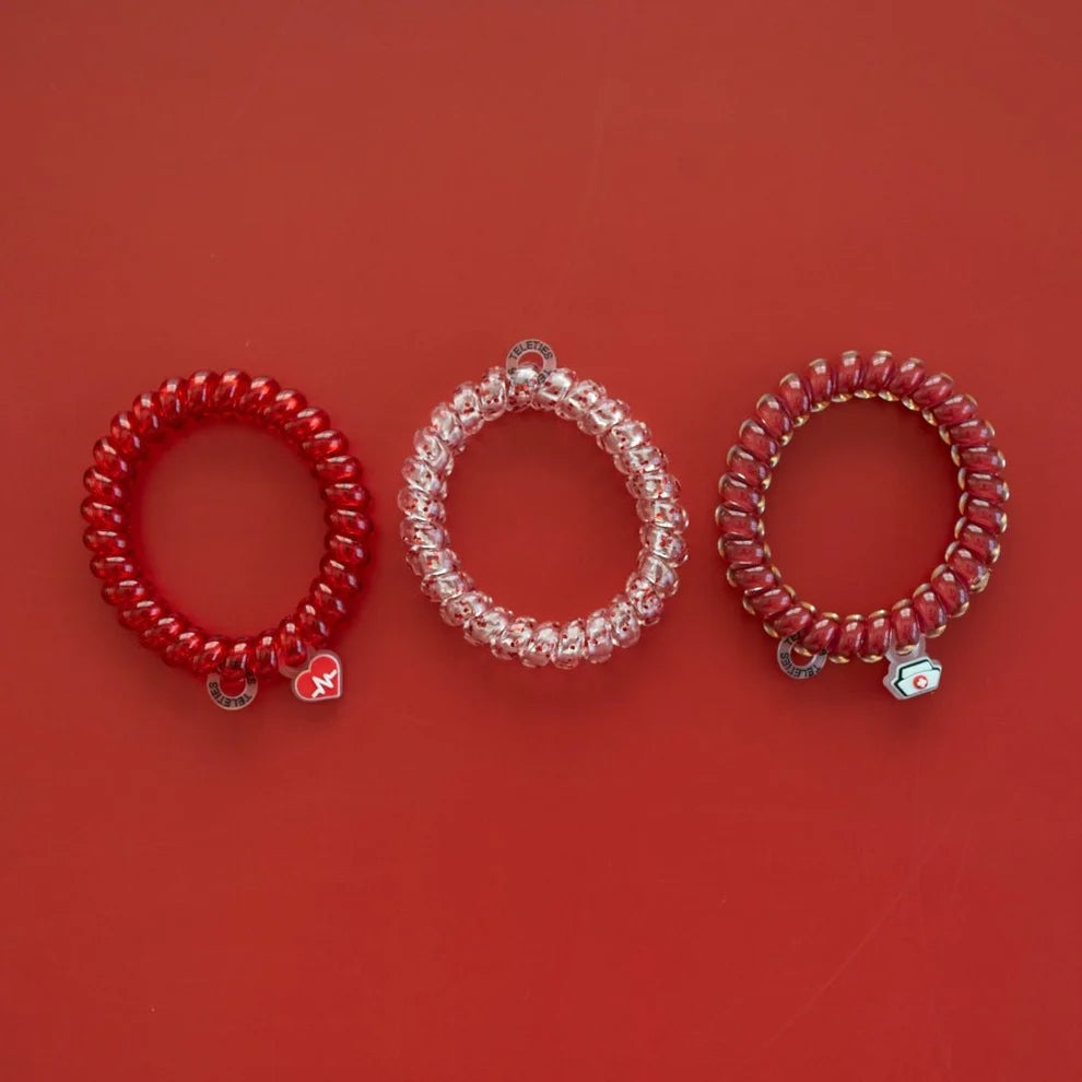 Three coiled elastic bracelets in red, clear, and dark red with small silver-toned charms, arranged on a solid red background.