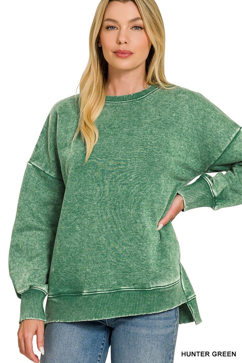A woman modeling a green oversized crewneck sweatshirt with a washed, textured finish, paired with blue jeans against a plain white background.