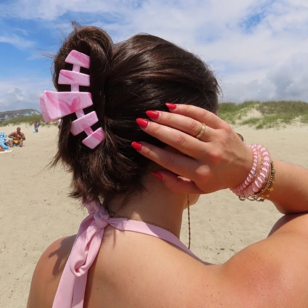 Person on a beach with pink hair clip and bracelet, wearing a pink top.