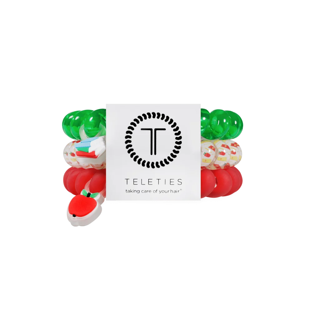 A Teleties hair care set featuring multiple colorful silicone hair ties and a white central card with the Teleties logo and the text 'taking care of your hair'. The set includes solid green, solid red, patterned white with red and green details, and a red-and-white strawberry design.