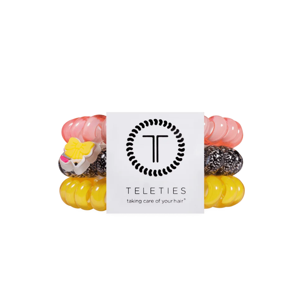 A set of four Teleties hair tie bracelets wrapped together with a white paper band. The bracelets are translucent pink, yellow, and black speckled, with one pink and one yellow bracelet featuring a small animal charm.