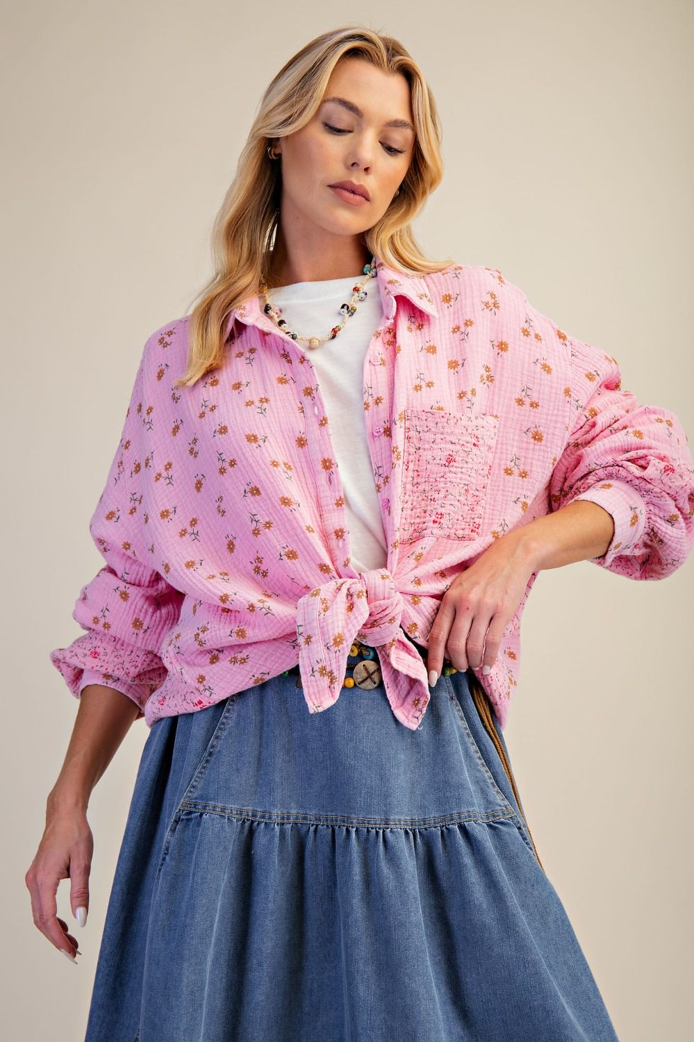 Woman wearing a pink floral blouse and blue skirt against a beige background