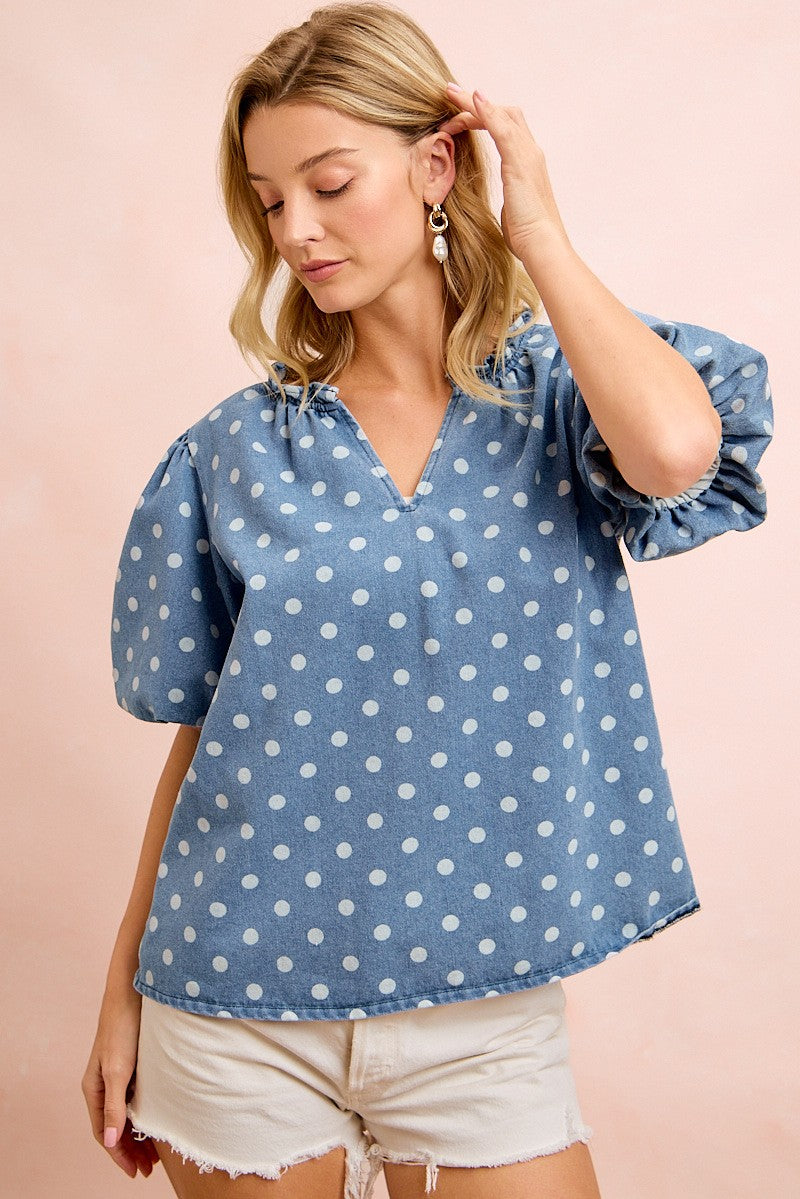 Woman wearing a blue polka dot blouse with puff sleeves on a pink background