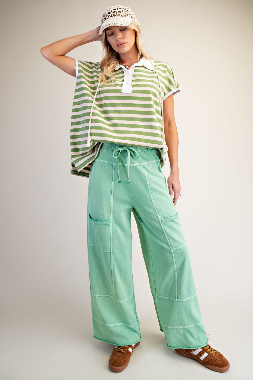 Woman wearing green and white striped top and apple green mineral wash pants. With a beige background.