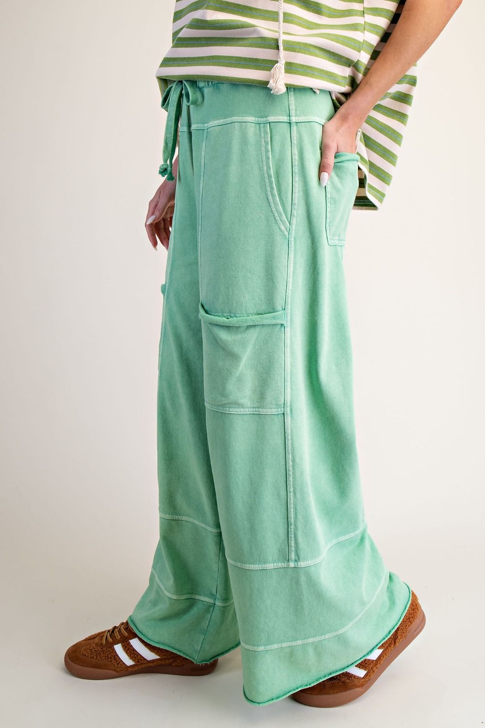 Woman wearing green and white striped top and apple green mineral wash pants. With a beige background.