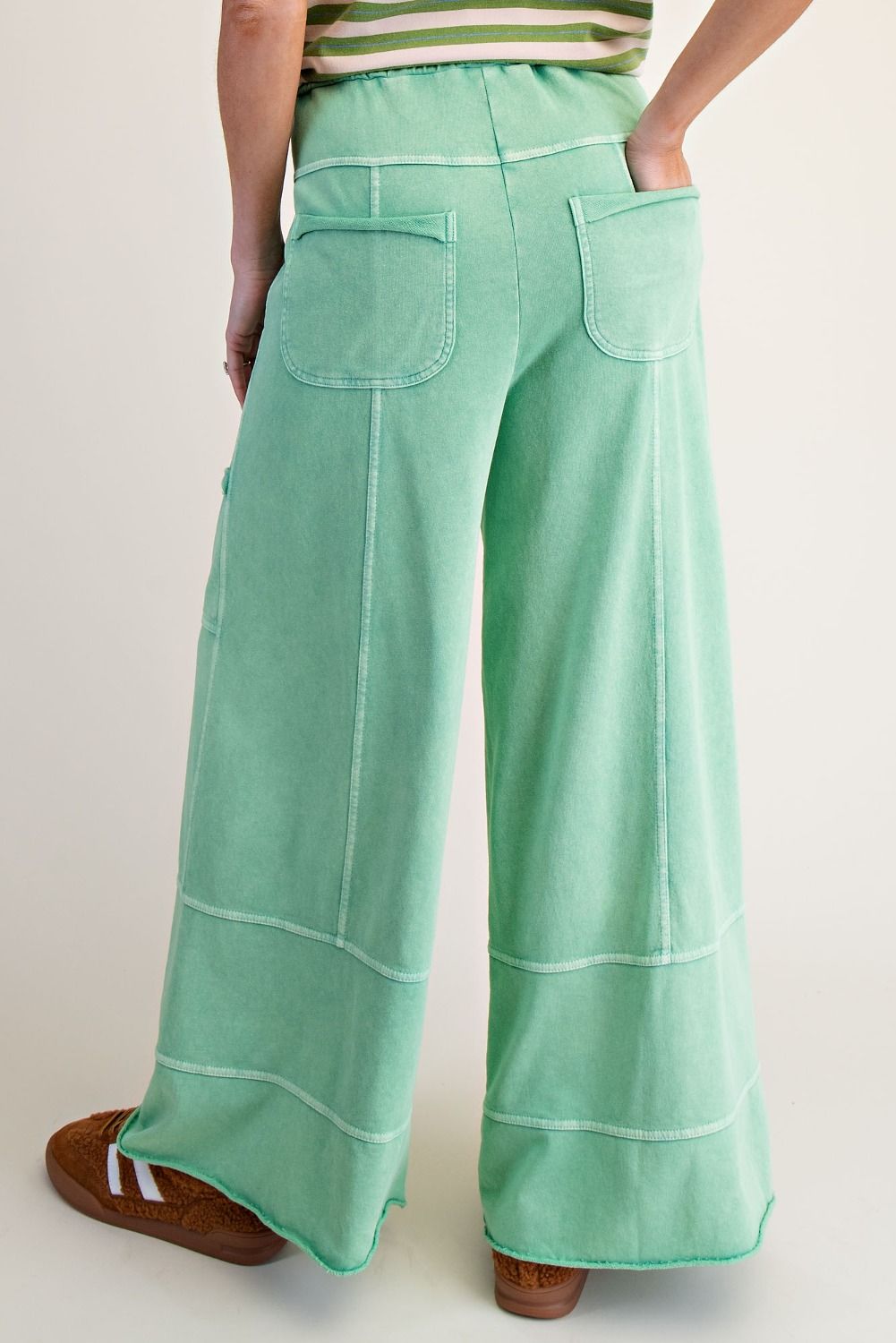 Back of a woman wearing green and white striped top and apple green mineral wash pants. With a beige background.