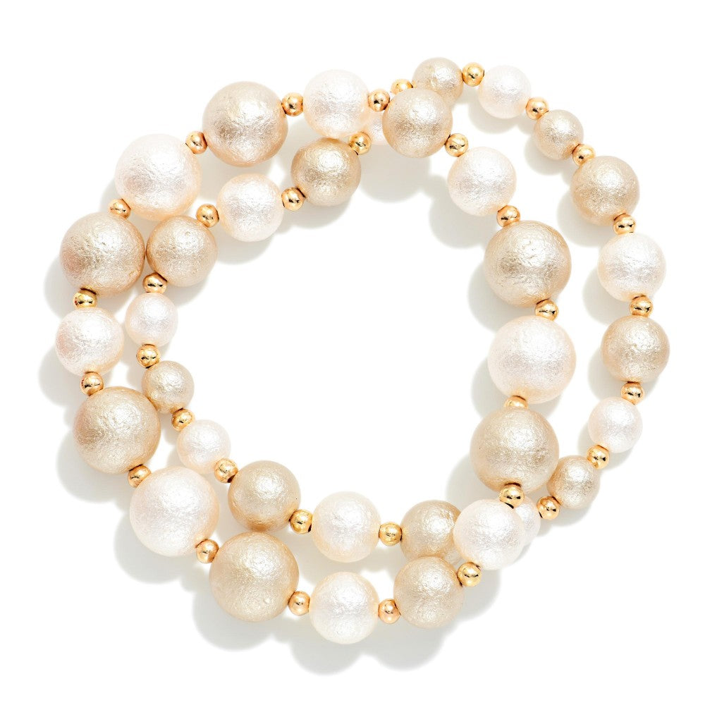 A double-strand beaded stretch bracelet featuring textured champagne-gold and white faux pearls separated by small metallic gold spacer beads, shown on a clean white background.