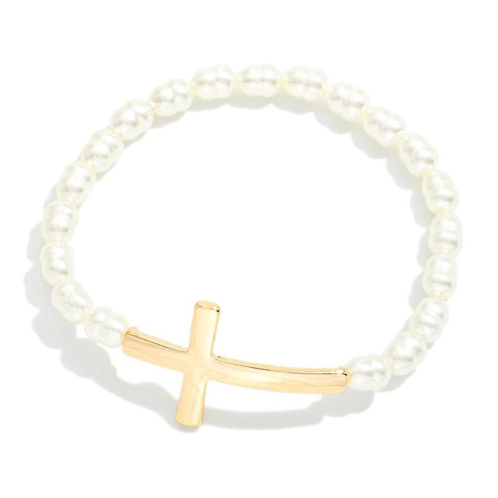 A beaded stretch bracelet featuring white pearl-like beads and a polished gold cross charm, displayed on a clean white background with a soft shadow.
